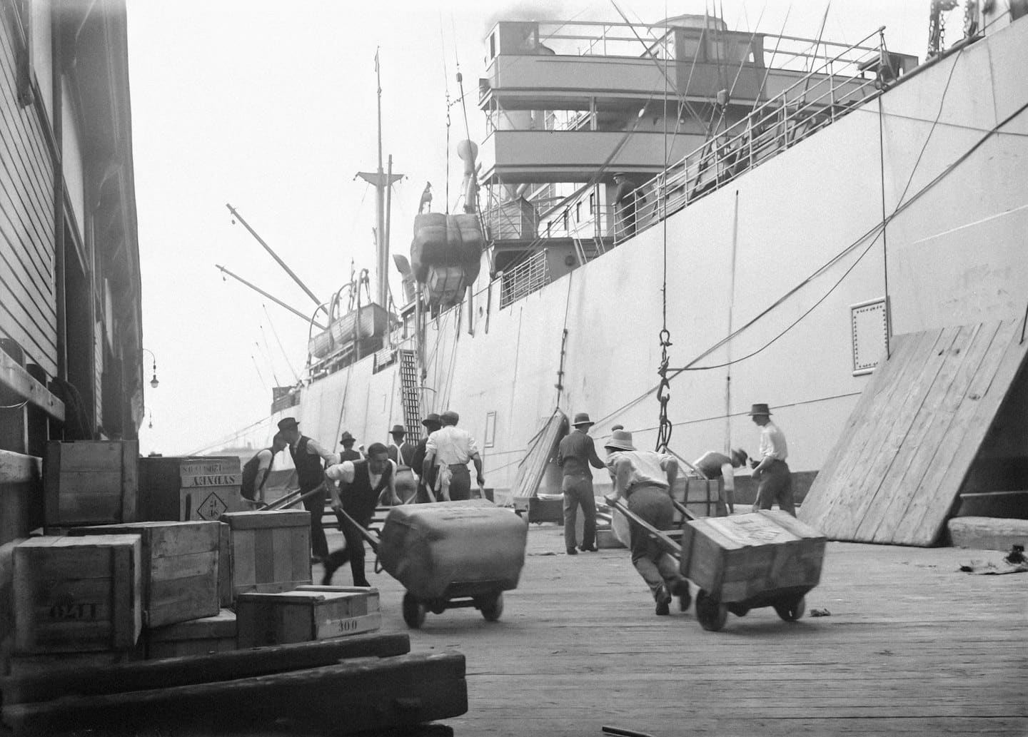 Dock workers load wooden crates onto a large cargo ship.